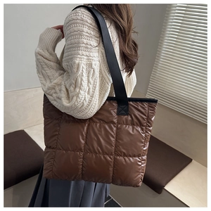 Brown quilted puffer tote bag with black strap shown on shoulder in minimalist interior