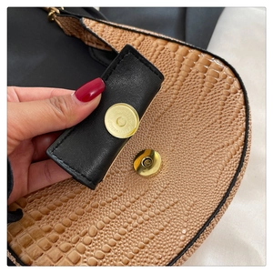 Detail of gold magnetic clasp on crocodile texture two-tone crescent bag