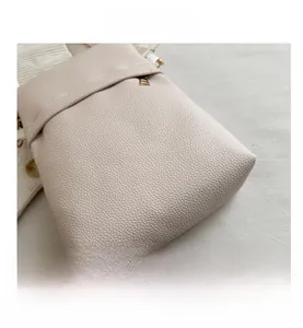 Macro shot of cream pebble leather texture and metal zipper detail on the crossbody bag