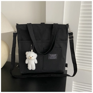Detail of black canvas tote bag showing fashion instinct label and plush bear charm