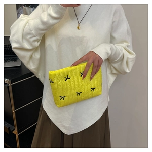 Detail of yellow quilted clutch bag with black bow embroidery held by a model