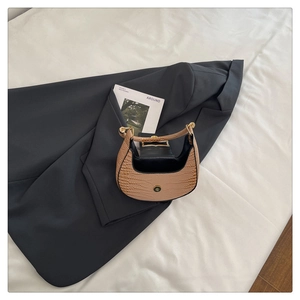 Top view of a beige crescent bag with crocodile texture on a grey suit background