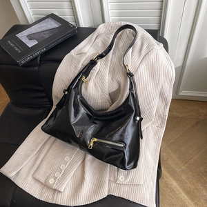 Glossy black patent leather hobo bag with gold hardware on beige corduroy jacket
