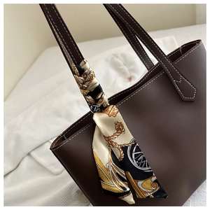 Close-up of deep brown tote bag handle with elegant silk scarf and white stitching