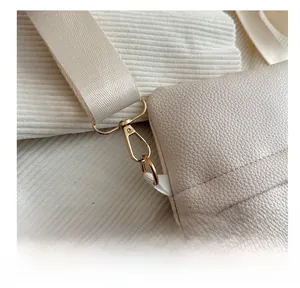 Detail of beige lychee leather bag featuring a wide fabric strap and gold metal hook