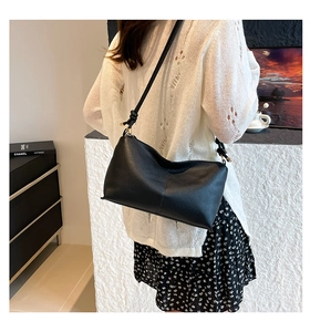 Detail of black pebbled leather crossbody bag with knot strap and gold hardware accents