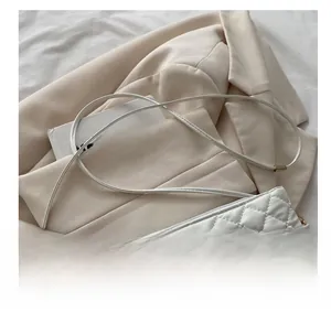 Détail du sac à bandoulière matelassé blanc avec boucle nœud doré sur blazer crème