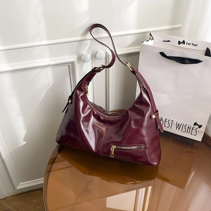 Burgundy faux leather crescent tote bag with glossy finish and gold zipper detail