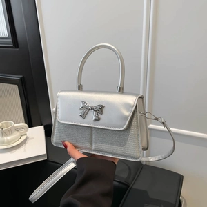 Silver metallic bow handbag with sequins and top handle, showing crossbody strap design