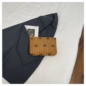 Brown quilted clutch bag featuring black bow embroidery placed on a blazer and magazine