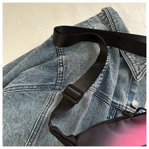 Détail d'un sac bandoulière dégradé rose et noir posé sur une veste en jean bleue