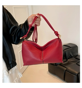 Close-up of red leather handbag featuring a knotted shoulder strap and gold hardware accents