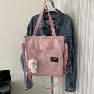 Pink canvas tote bag with dual handles and bear charm displayed on denim jacket