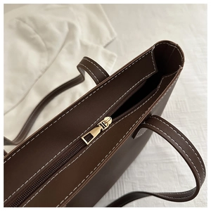 Detail of dark brown tote bag showing golden zipper closure and white contrast stitching