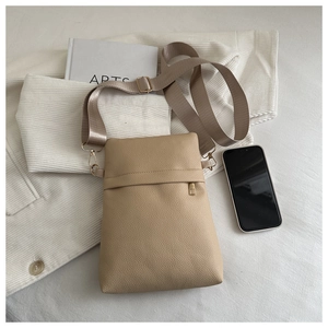 Detail of beige lychee pattern leather phone bag with adjustable strap on white bedding