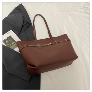 Flat lay of a dark brown faux leather tote bag with gold buckle on white fabric