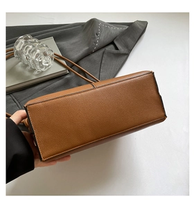 Detailed bottom view of brown lychee grain leather handbag with black edge coating