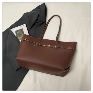 Detail of a brown leather tote bag with gold buckle on a stylish office flat lay