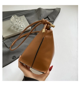 Detail of brown lychee grain leather handbag with gold metal hardware and knotted strap