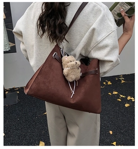 Detail of dark brown suede tote bag with drawstring and cute bear charm in outdoor setting