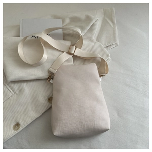 Close-up of cream textured leather crossbody bag with wide strap on striped shirt