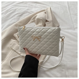 Détail du sac matelassé blanc avec ornement nœud doré et fermeture éclair métallique