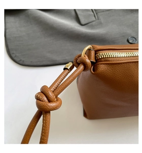 Detail of brown lychee texture leather shoulder bag with gold zipper and knotted strap