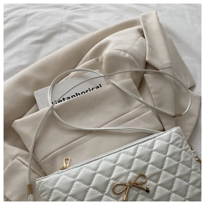 Détail du sac bandoulière blanc matelassé avec nœud doré sur un blazer beige élégant