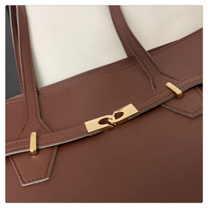Detailed close-up of brown leather tote bag with light gold metal clasp and fine stitching