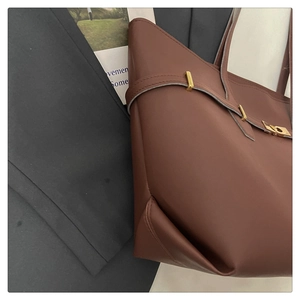 Detail of a brown leather tote bag showing fine texture and golden metal buckle