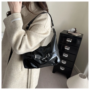Close-up of black patent leather underarm bag with silver hardware on a wool coat