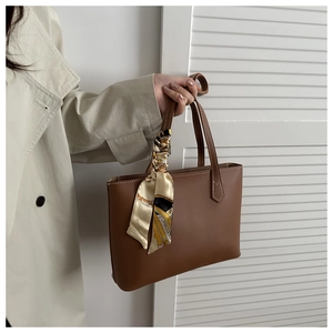 Brown leather tote bag with elegant silk scarf detail held by a model in a trench coat