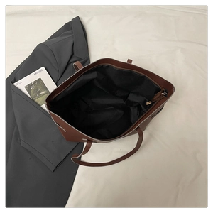 Detail view of brown faux leather tote bag with zipper closure and black fabric lining
