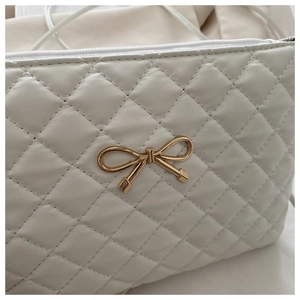 Gros plan du sac matelassé crème avec nœud doré et texture en losanges raffinée