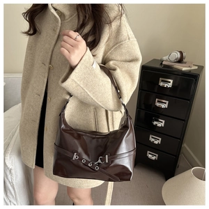 Detail view of dark brown glossy leather underarm bag with metallic eyelet strap decor