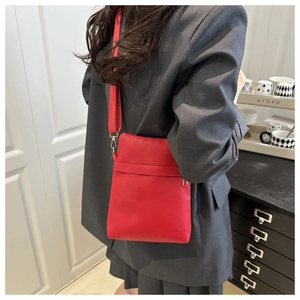 Detail of red pebbled leather crossbody bag with adjustable strap and gold metal hooks