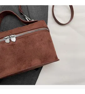 Detail view of brown suede crossbody bag featuring unique double heart-shaped metal zippers