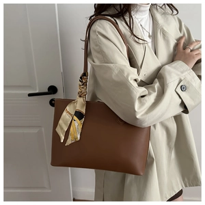 Brown faux leather tote bag with decorative patterned silk scarf shown on a beige coat