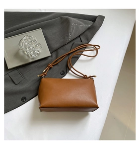 Detailed view of brown leather bag with elegant knotted strap design on white surface