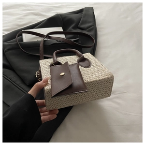 Detail of woven straw handbag featuring brown leather handles and small envelope charm