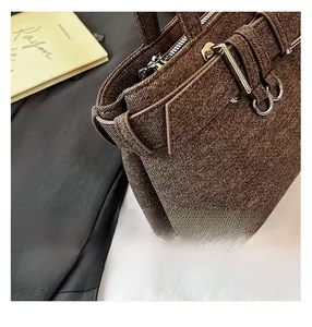 Close-up of textured brown fabric handbag with silver zippers and metal buckles