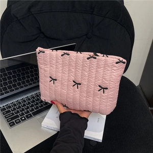 Pink quilted clutch with embroidered black bows shown in a stylish lifestyle setting