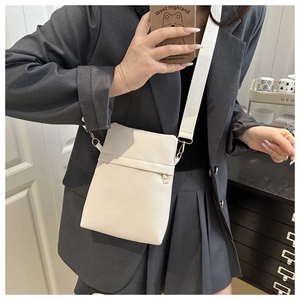 Detail view of a white pebbled leather crossbody bag with a wide woven strap and gold zip
