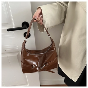 Detail of a dark brown glossy leather underarm bag with silver hardware on a beige trench coat