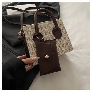 Detail of woven straw tote bag featuring brown faux leather trim and mini pouch attachment
