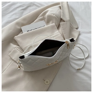 Détail d'un sac bandoulière blanc matelassé avec nœud doré et texture de couture élégante