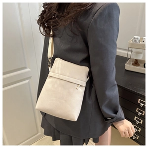 Detail of cream crossbody bag with pebble leather texture and fabric strap on model