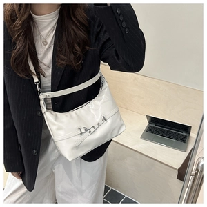 Hobo bag detail showing white glossy leather with silver buckle and wide strap on model