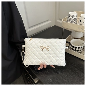 Détail d'une pochette blanche matelassée avec nœud doré et dragonne de poignet