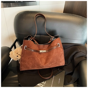 Detail of brown suede tote bag with leather straps, silver lock, and plush bear charm